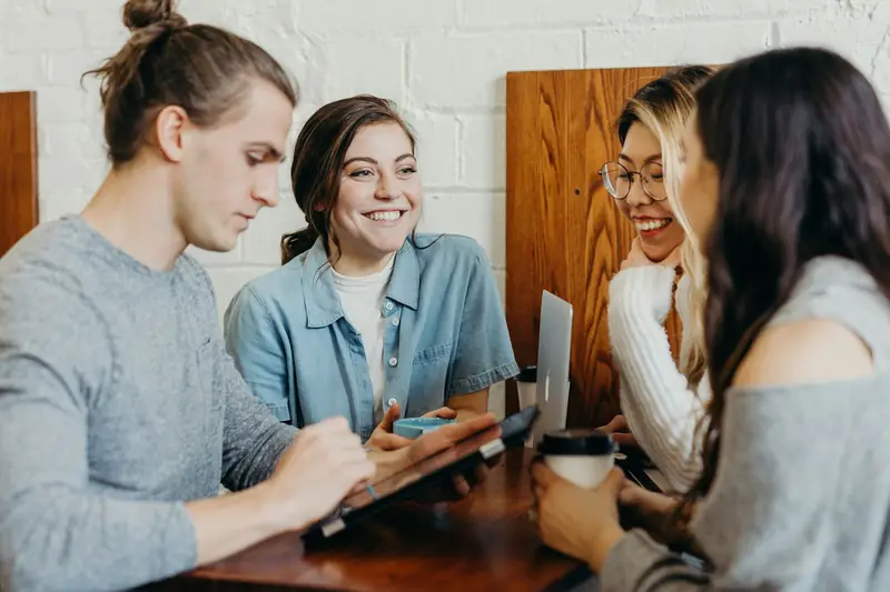 Four colleagues smiling and talking around a table with laptops and coffee