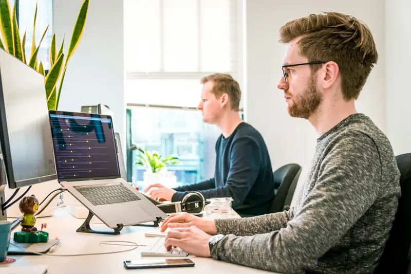 Two engineers working side by side at desks with large monitors