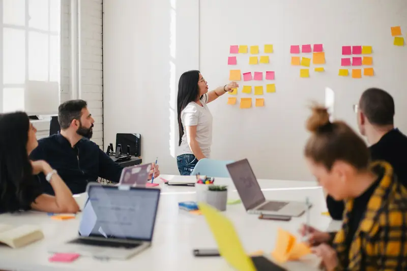 Participants in a workshop discuss ideas while a facilitator arranges sticky notes on a wall